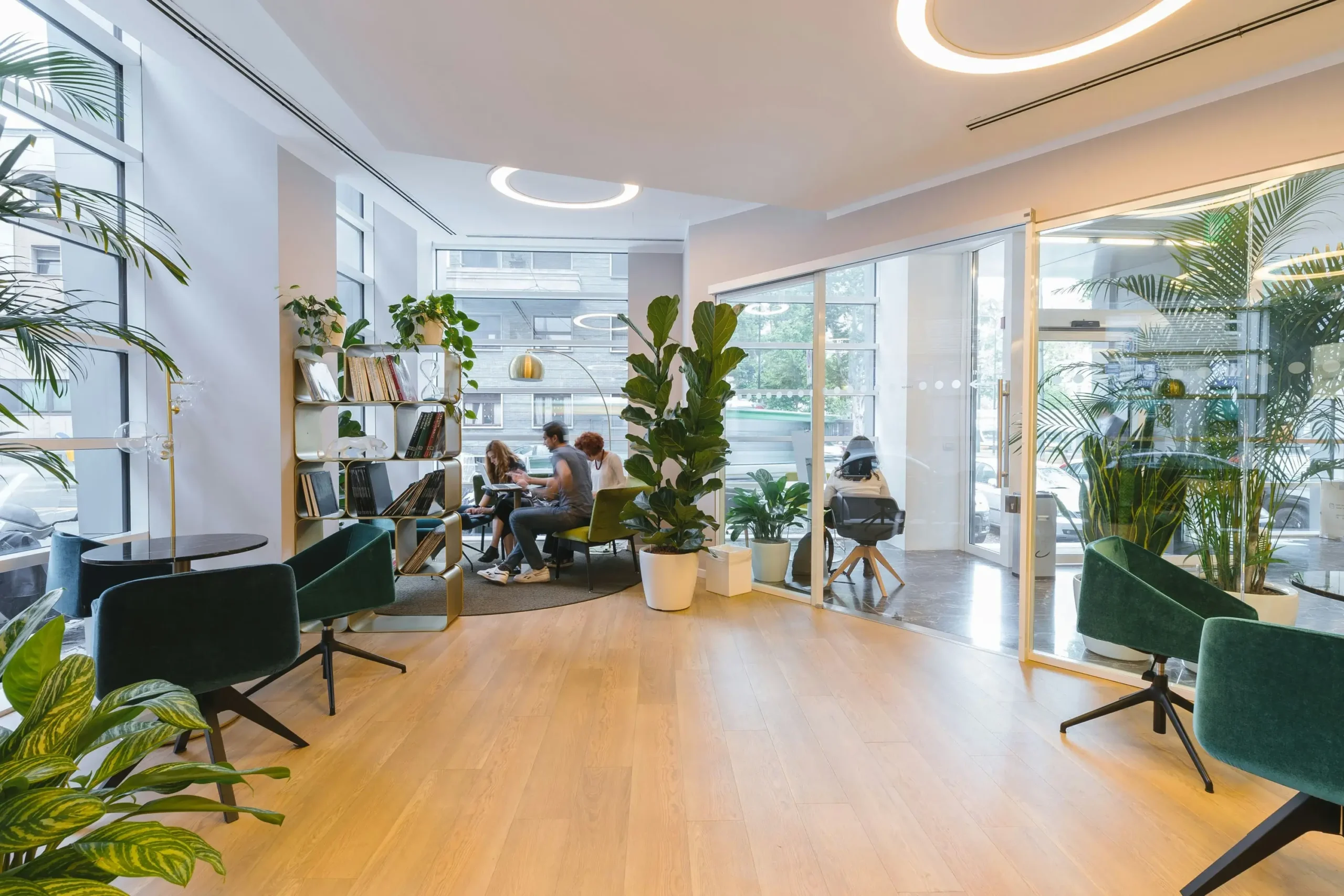 Helles, modernes Büro mit großen Fenstern, grünen Pflanzen und Menschen, die an Tischen zusammenarbeiten.