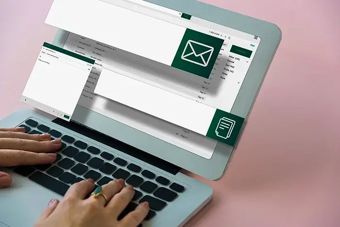 Hände tippen auf der Tastatur eines Laptops, auf dessen Bildschirm eine E-Mail-Anwendung geöffnet ist.