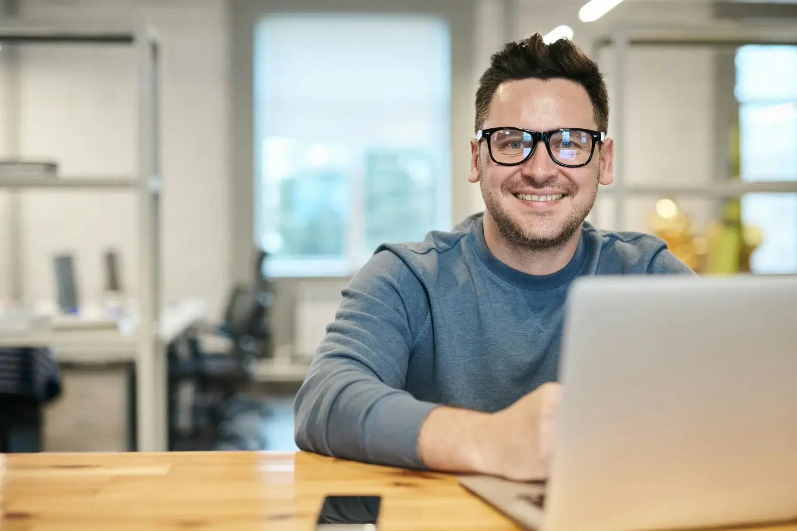 Lächelnder Mann mit Brille sitzt am Computer in einem hellen Büro